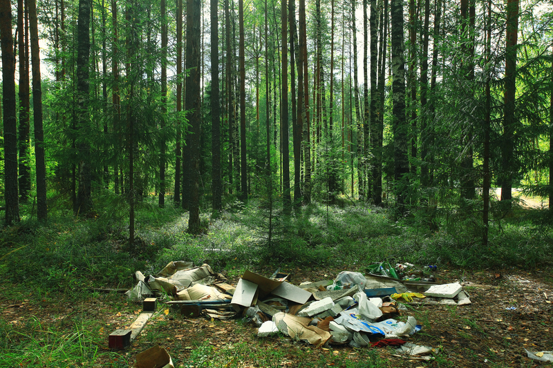 Person flattening cardboard boxes and labelling indoor recycling containers in a hallway.